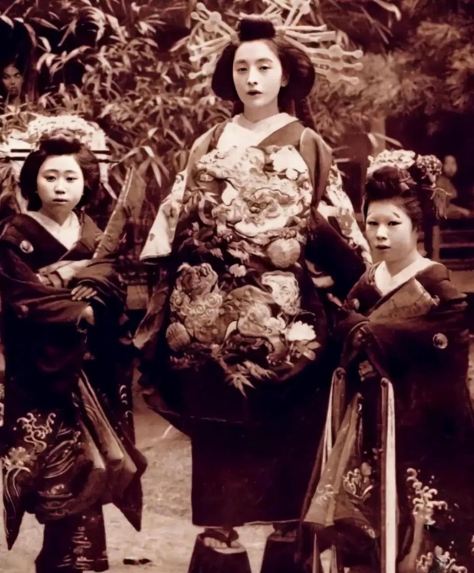 #历史那些事[超话]#旧时日本一张花魁的老照片，她扎着一个复杂的发髻，旁边还有两