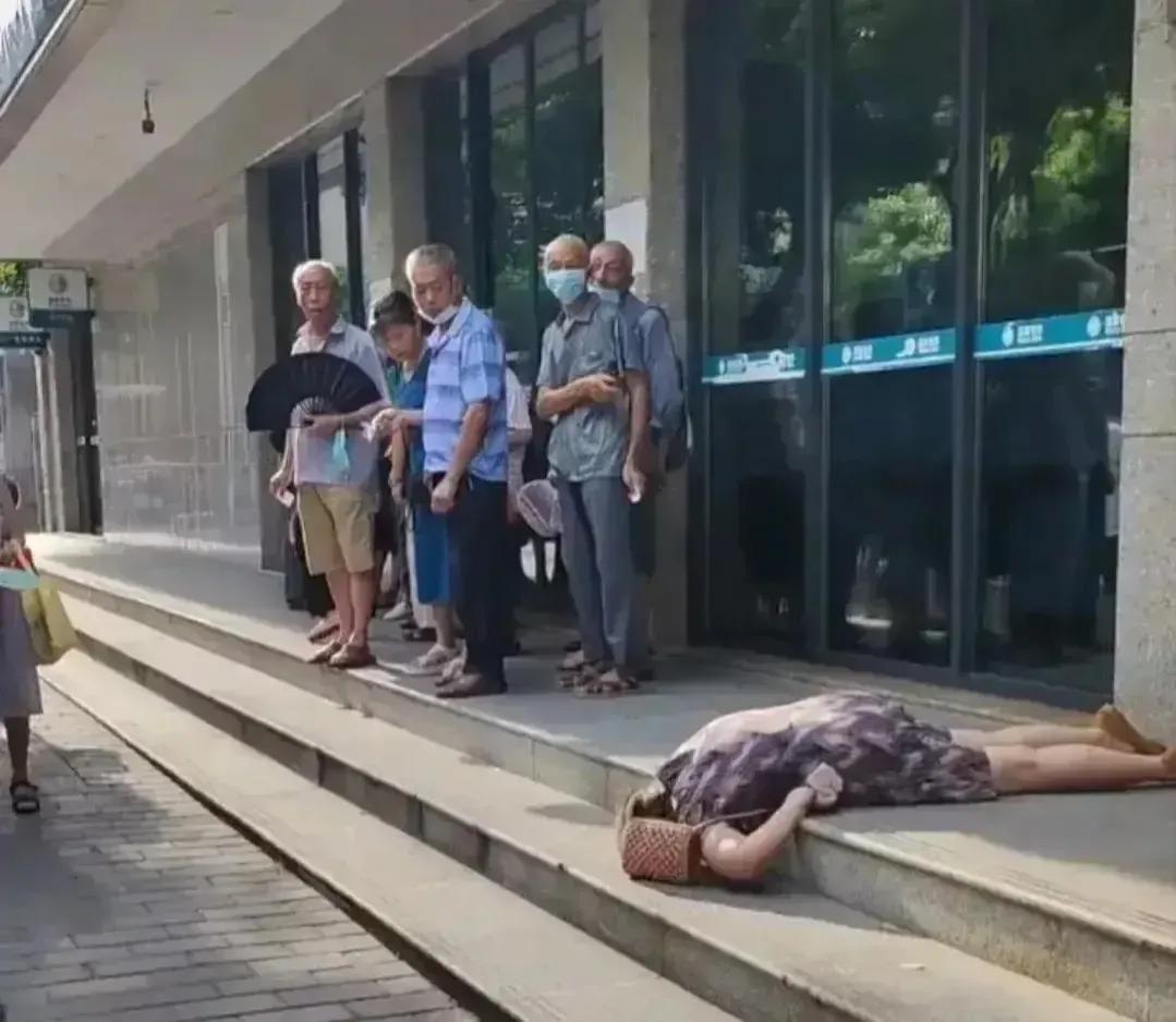 一个年约50岁的女子突然晕倒在地。她的脸色发白，双手无力地摊在地上，旁边的人们纷