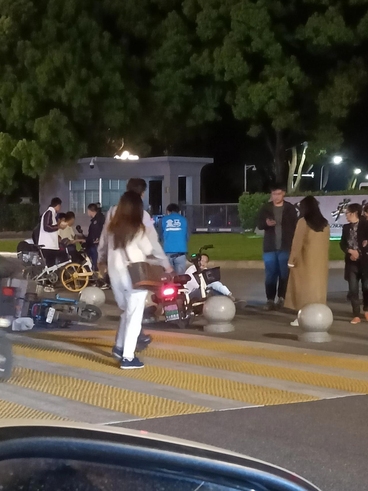  华中科技大学门口，一位盒马小哥的电动车与另一辆电动车发生了碰撞。穿白衣的倒地后