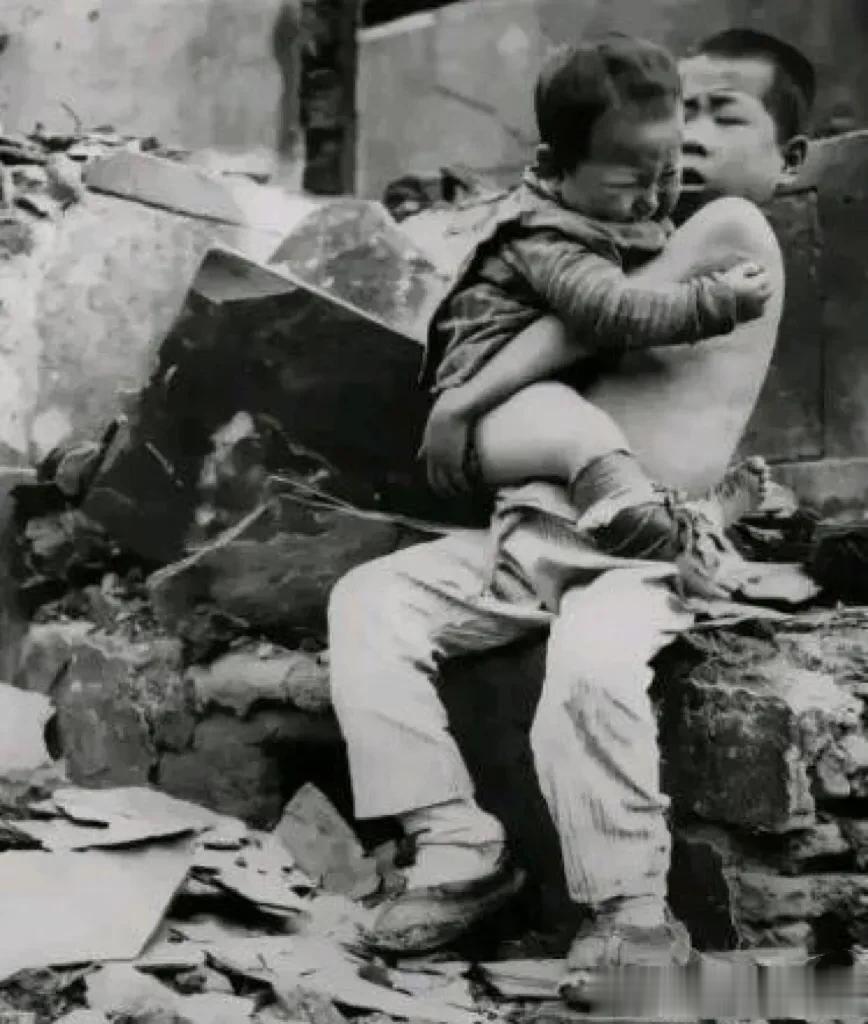 1943年，一名5岁的男孩抱着年幼的弟弟，在他们周围是被日军轰炸后的废墟，他们的