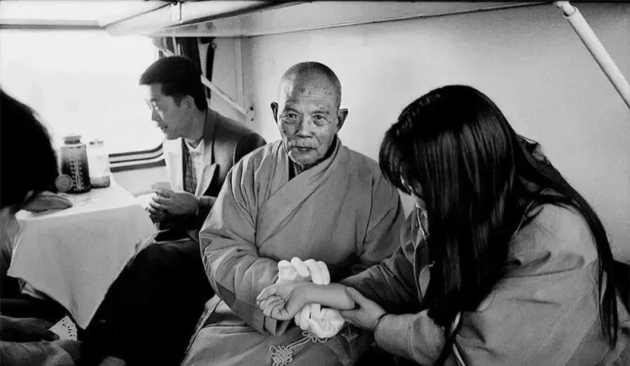 上世纪80年代，绿皮火车车厢里，一位老和尚正在给一个姑娘把脉。
可以看到这个老和
