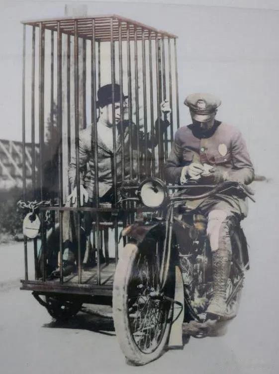 1921年，美国。
一名嫌疑人坐在用边三轮摩托车改装的警车笼子里，旁边的警察在做