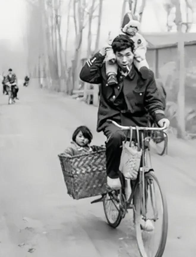 上世纪80年代，一个年轻父亲骑着自行车驮着俩孩子，车技高超，就像玩杂技。
这个年