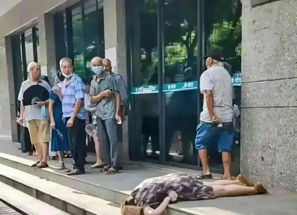 一位中年女人倒在银行门口，旁边一众大爷叼烟围观，离开一米多远，没有一个人上前搀扶