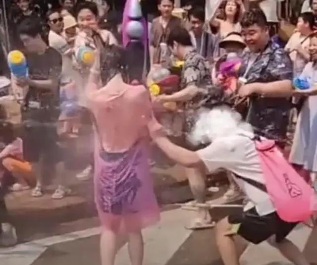 女子泼水节被众男子围着泼水撕雨衣，十分无奈。

山东淄博烧烤、云南泼水节、广西三