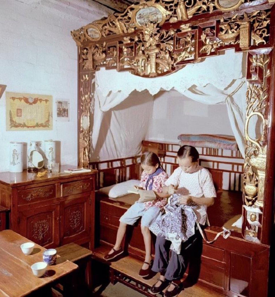 50年代一小女孩和母亲坐床沿的情形，她们背后的床是亮点，过去应该非富即贵。这张床